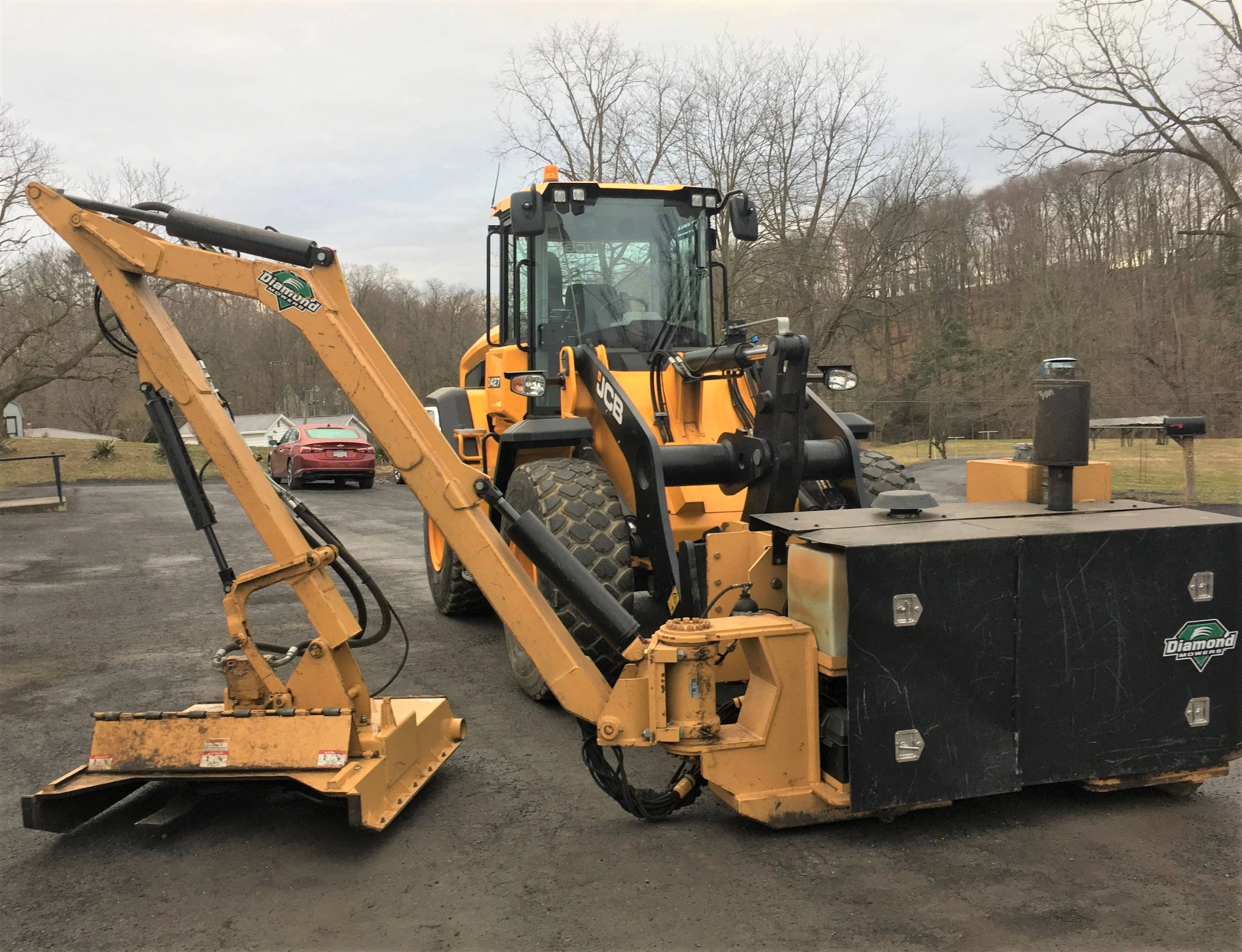 A piece of construction equipment with an attached brush loader sits in a parking lot.